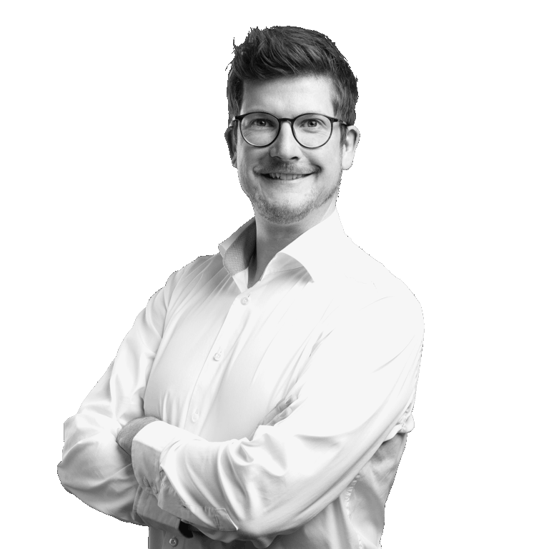 Porträt von Marcel Cornelius lächelnden mit Brille in einem weißen Hemd vor hellem Hintergrund.