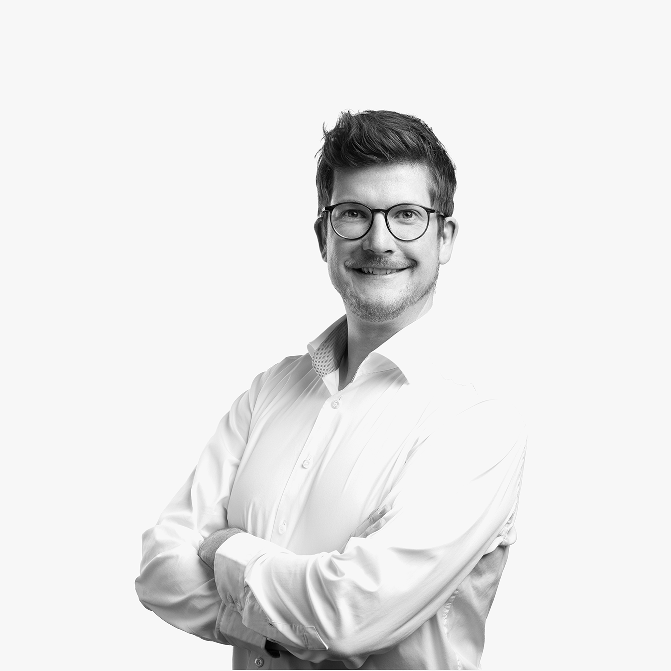 Porträt von Marcel Cornelius lächelnden mit Brille in einem weißen Hemd vor hellem Hintergrund.